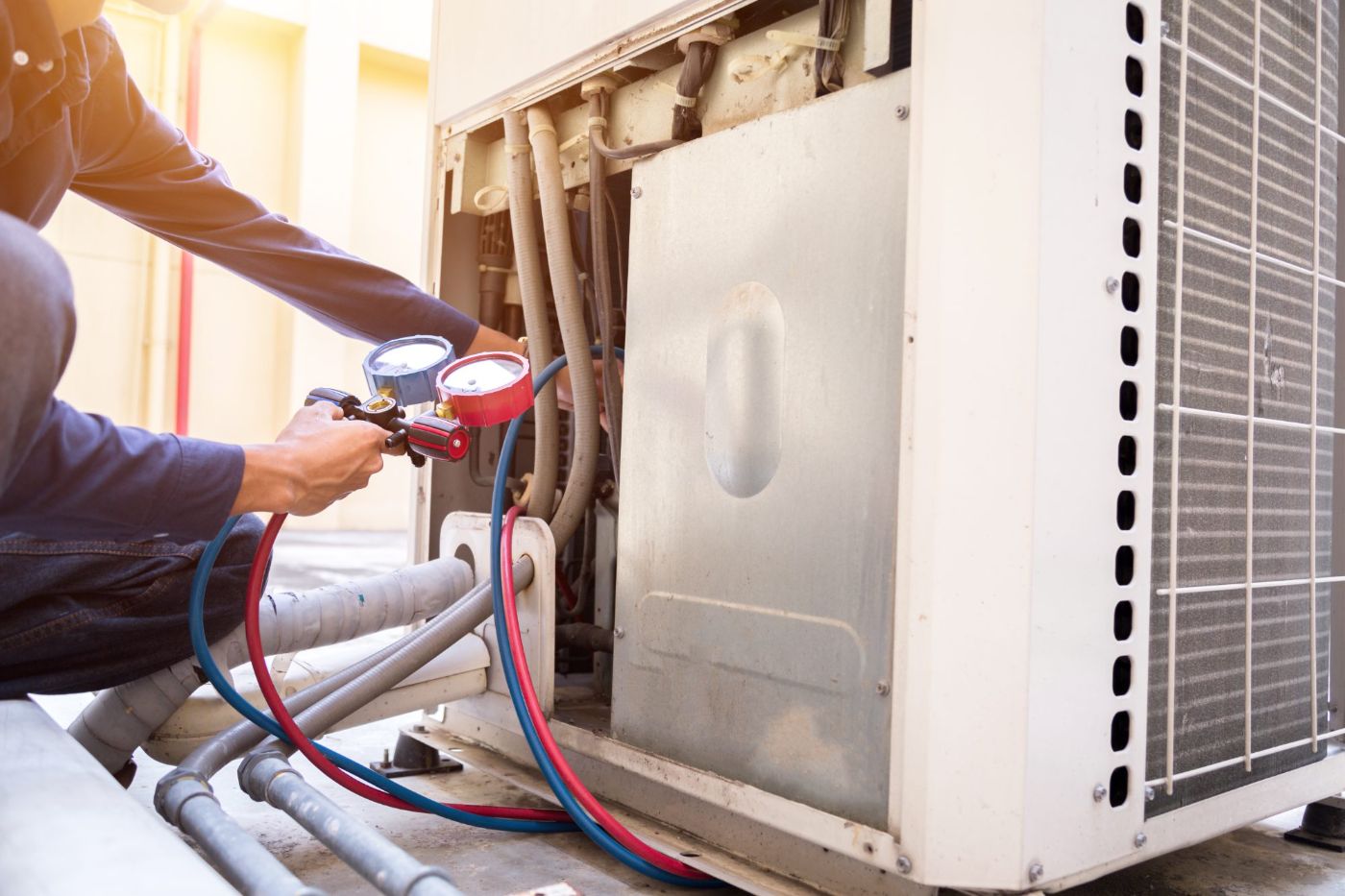 HVAC technician using manifold gauges to service outdoor air conditioning unit