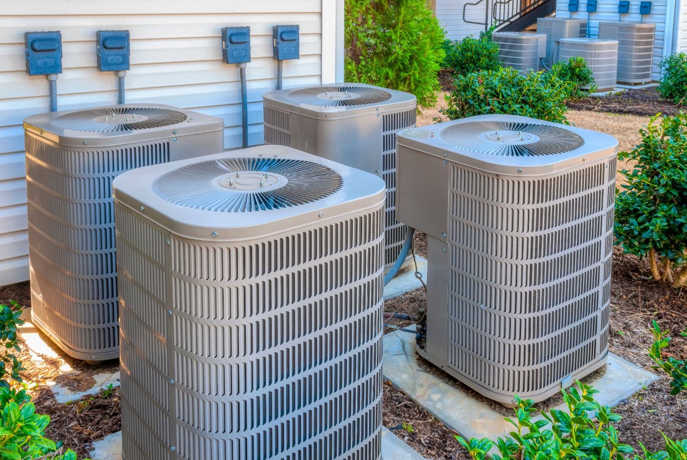 Multiple outdoor air conditioning units installed against a residential house exterior