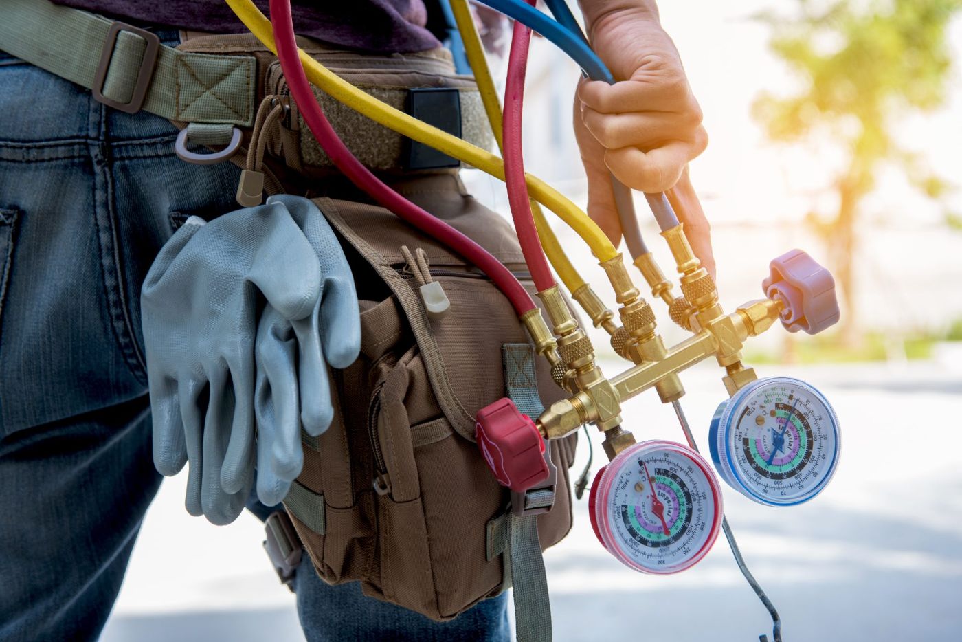 HVAC technician holding manifold gauges and wearing work gloves and tool belt