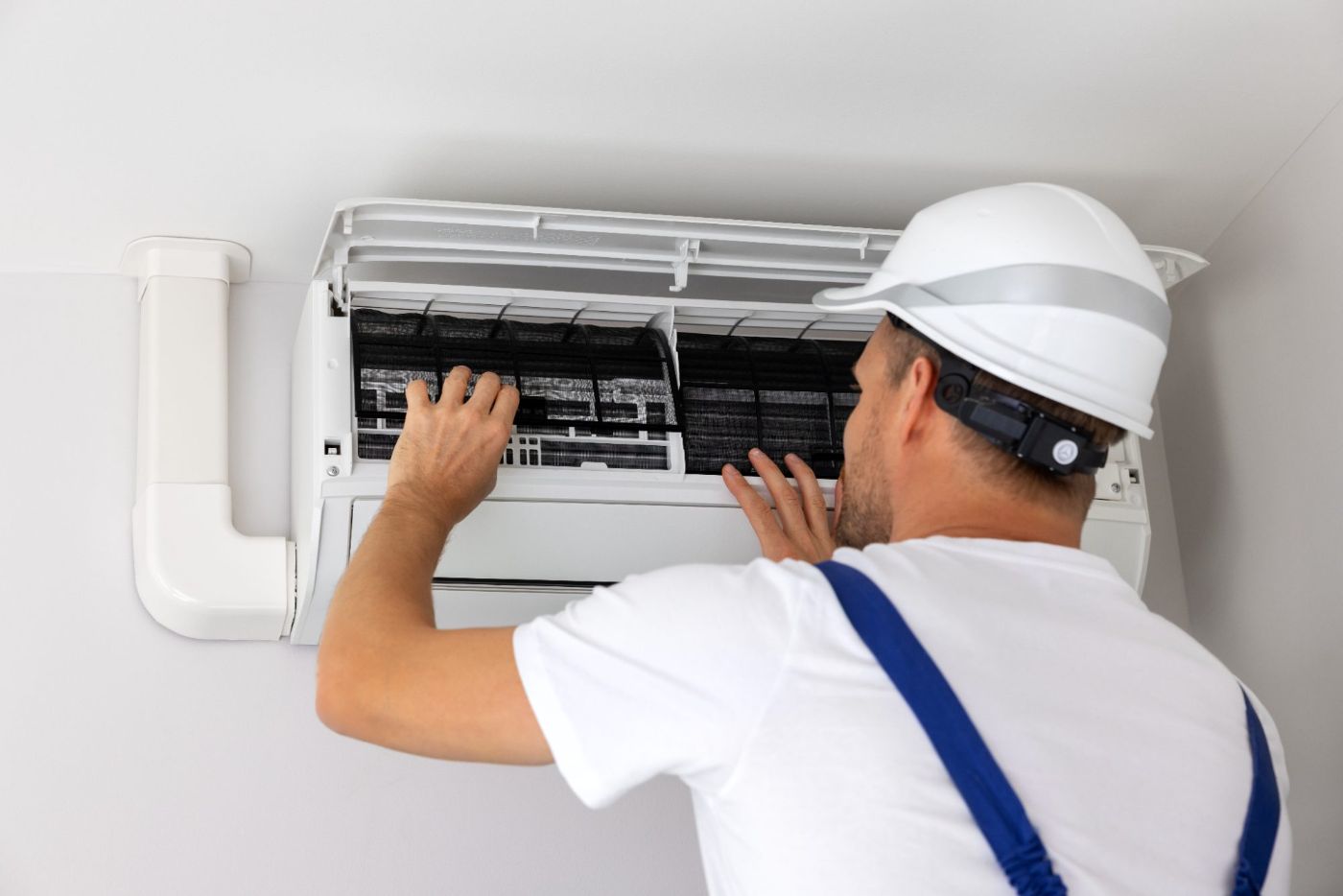 Technician in white hard hat inspecting air conditioning unit filter indoors